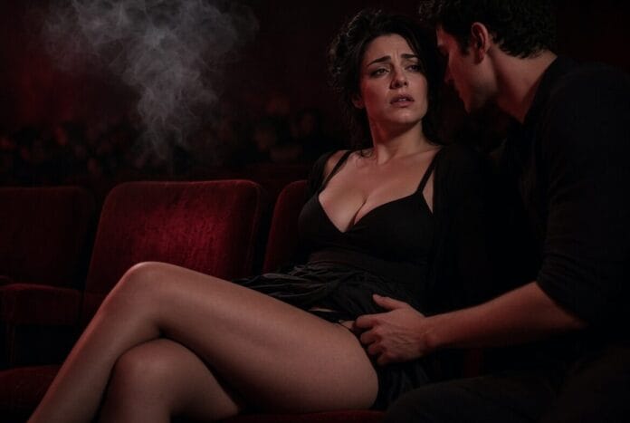 Una donna in abito nero seduta sulle poltrone del cinema con un uomo accanto in una sala buia.