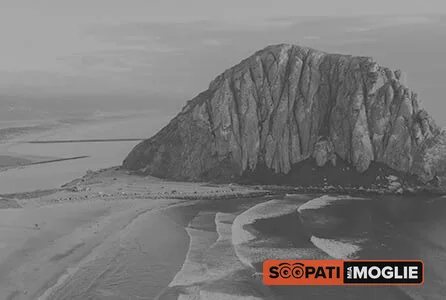 Una grande roccia si erge sulla spiaggia sabbiosa bagnata dalle onde del mare sotto un cielo nuvoloso.