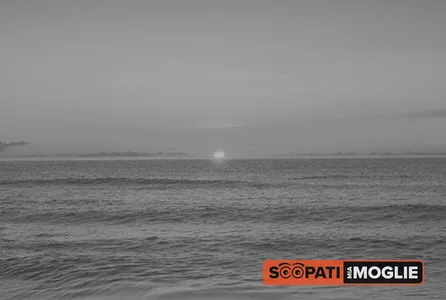 Paesaggio marino all'alba ripreso in tonalità di grigio con il sole basso sull'orizzonte e onde leggere