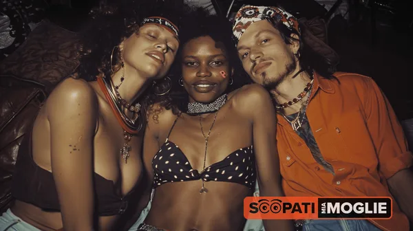 Due donne e un uomo sorridono abbracciati in un ambiente scuro illuminato da luce calda.