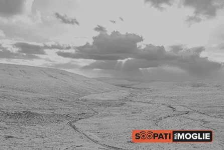 Un paesaggio collinare desolato in bianco e nero sotto un cielo nuvoloso con raggi di luce